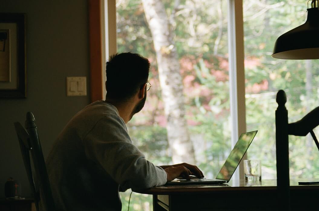 A person stares out of their window while working from their kitchen table, potentially considering their next career move.